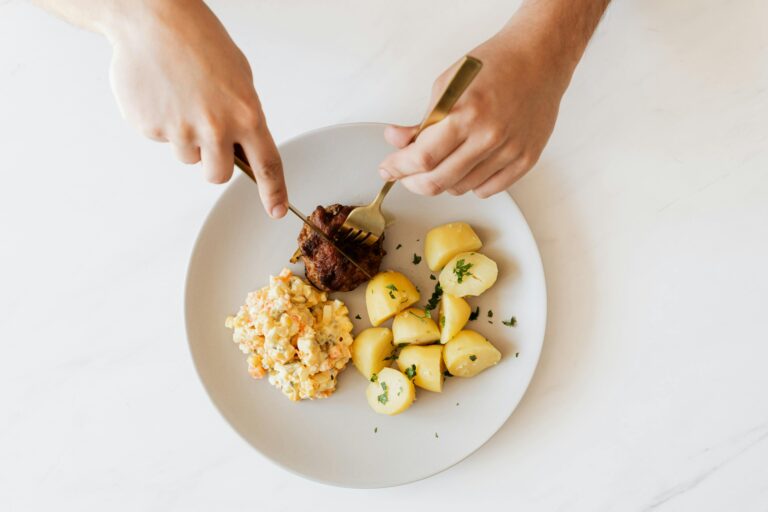 Crop man cutting cutlet on plate with salad and potatoes